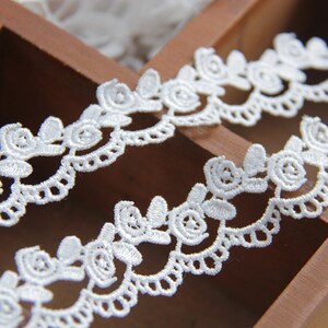 May include: White lace trim with a delicate floral pattern. The lace is made of a fine, soft material and has a scalloped edge.