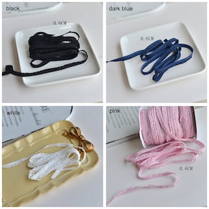 Pu&ograve; includere: Quattro bobine di passamaneria elastica arricciata in nero, blu scuro, bianco e rosa. Ogni bobina &egrave; larga 0,6 cm.