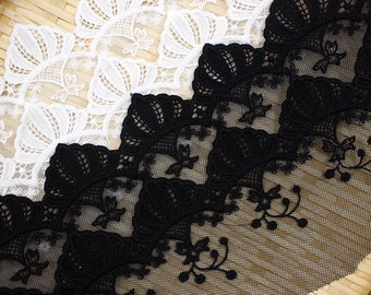 Peut inclure: Gros plan sur un tissu en dentelle blanche et noire. La dentelle présente un motif floral et en éventail détaillé. Le tissu est disposé en diagonale, mettant en valeur le design et la texture complexes de la dentelle.