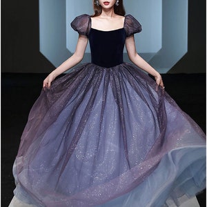 K&ouml;nnte beinhalten: Ein blaues und violettes Ombre-T&uuml;ll-Ballkleid mit einem Samt-Oberteil und Puff&auml;rmeln. Das Kleid hat ein glitzerndes Finish.