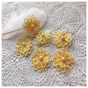 Könnte beinhalten: Sechs gelbe Stoffblumen mit einem Perlenkern. Die Blumen sind geschichtet und haben eine zarte, spitzenstichelartige Textur.