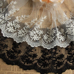 May include: Two rolls of delicate floral lace trim. One roll is white and the other is black. Both rolls have a scalloped edge and a floral design.