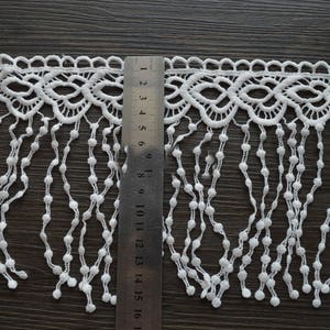 May include: White lace trim with a scalloped edge and fringe. The fringe is made of small white beads and hangs approximately 40 cm long.