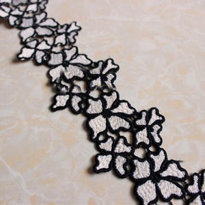 May include: White lace trim with black embroidery featuring a floral design.