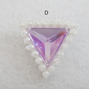 Może przedstawiać: Trójkątny, fioletowy, tęczowy kryształ z białą obwódką pereł.
