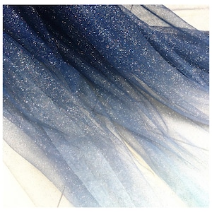 Op de afbeelding: Een blauwe tule stof met een gradiënt en glinsterende glitter. De stof is doorschijnend en heeft een zachte, vloeiende textuur.