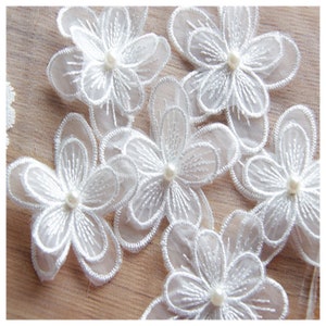 May include: White lace flower appliques with pearl centers. The appliques are layered and have a delicate, feminine look.