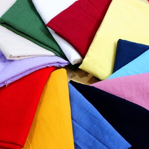 May include: A variety of fabric swatches in different colors, including red, yellow, blue, green, and pink. The swatches are arranged in a circle on a wooden surface.