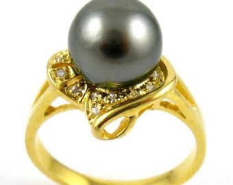 Puede incluir: Un anillo de oro con una gran perla negra y pequeños diamantes engastados en la banda.