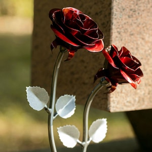 Puede incluir: Dos rosas de metal hechas a mano con un acabado rojo intenso brillante. Los pétalos están intrincadamente diseñados y los tallos son plateados. Las hojas son de color plata clara. Las rosas son un artículo decorativo.