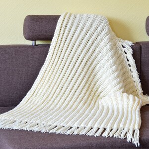 May include: A white crocheted throw blanket with fringe on a brown couch.
