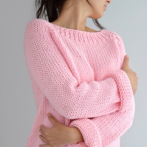 Puede incluir: Un su&eacute;ter de punto rosa de corte holgado y mangas largas. El su&eacute;ter est&aacute; hecho con un hilo grueso y tiene un dise&ntilde;o simple y cl&aacute;sico.