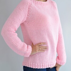 Puede incluir: Un su&eacute;ter de punto rosa con cuello redondo y mangas largas. El su&eacute;ter est&aacute; hecho de un hilo suave y grueso y tiene un ajuste holgado.