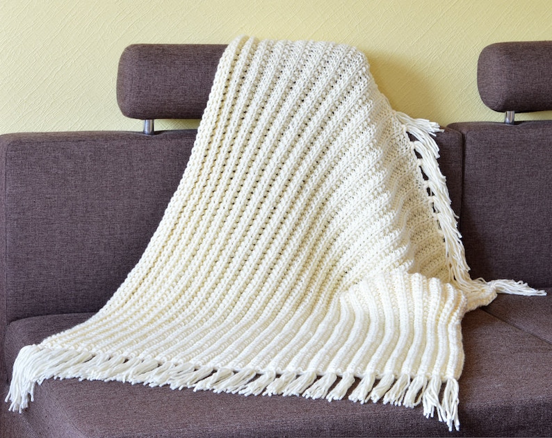 May include: A white crocheted throw blanket with fringe on a brown couch.