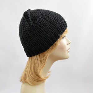 May include: A black knitted beanie with cat ears. The beanie is made of a soft, warm yarn and has a simple, classic design.