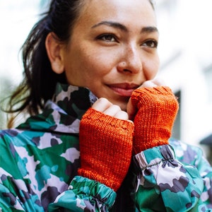 Könnte beinhalten: Eine Person trägt eine grüne Tarnjacke mit orangefarbenen fingerlosen Handschuhen.