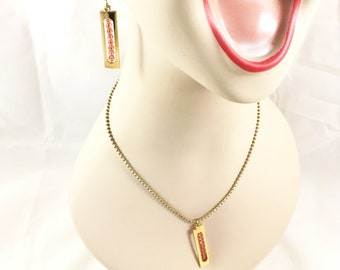 May include: A gold necklace and earrings set with a rectangular pendant and matching earrings. The pendant and earrings are filled with small, pink beads.