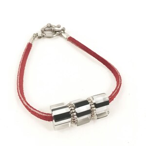 May include: A red suede bracelet with a silver clasp and three clear, rectangular beads with black and white stripes. The beads are separated by small silver rings. The bracelet is displayed on a white background.
