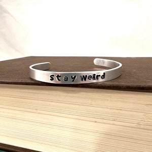 May include: A silver bracelet with the words "Stay Weird" engraved on it.