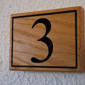 May include: A wooden sign with a black border and the number "3" carved into it.