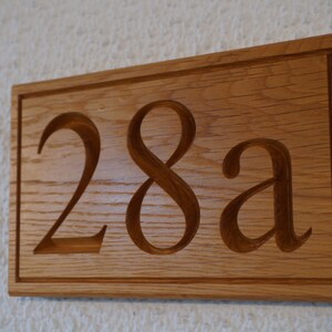 May include: A wooden house number sign with the number 28a carved into it.
