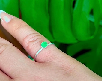May include: A silver ring with a small, round, bright green stone.