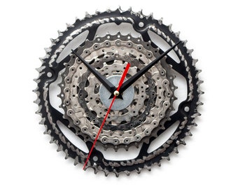 May include: A black and silver wall clock made from bicycle gears and chain. The clock has black hands and a red second hand.