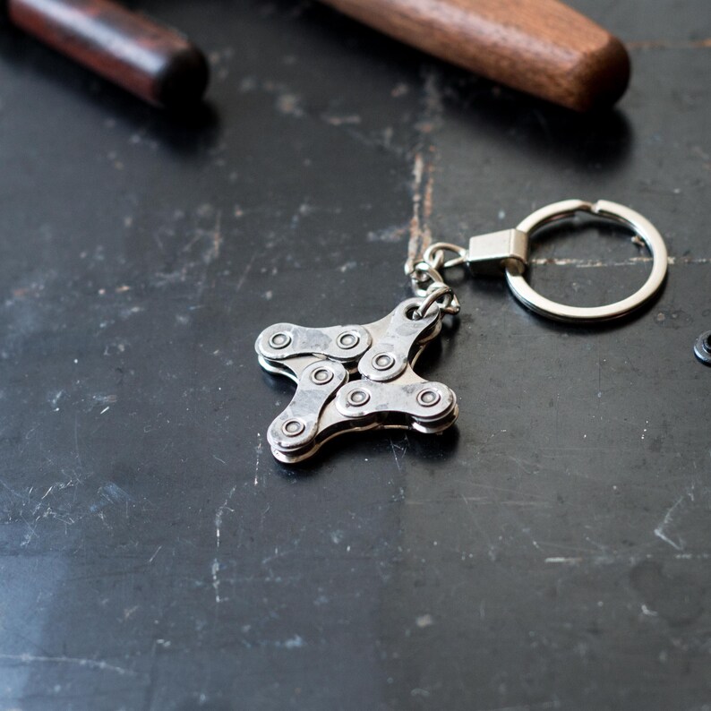 May include: A silver keychain shaped like a star, made from bike chain links. The keychain has a silver ring attached to it.
