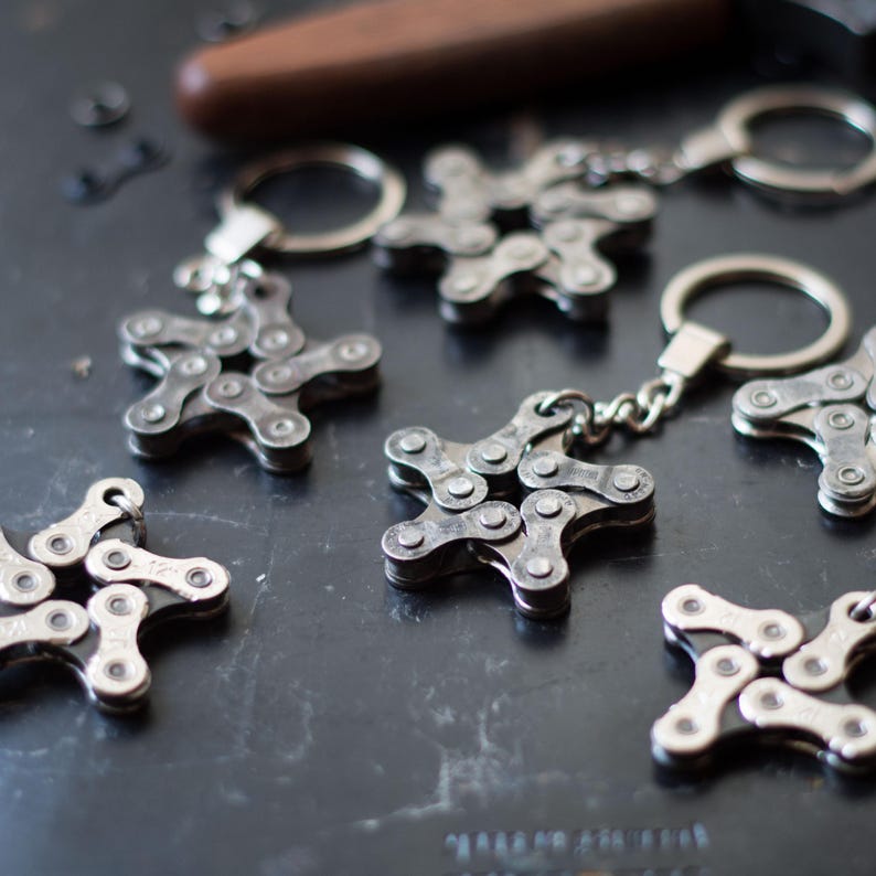 May include: A set of six silver star-shaped keychains made from linked bicycle chains. Each keychain has a silver ring attached to the top.