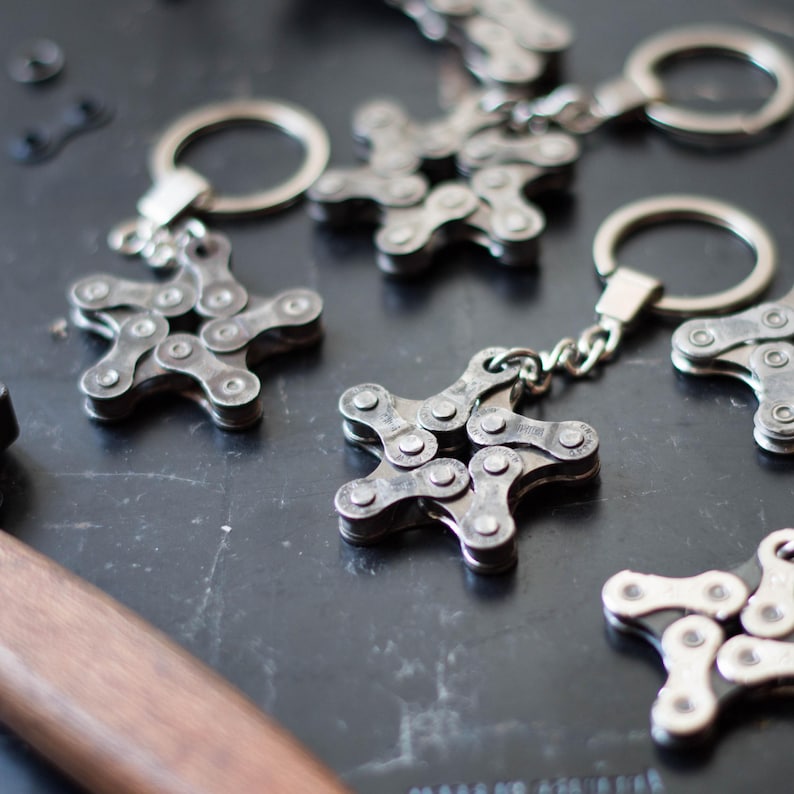 May include: A set of five silver star-shaped keychains made from linked bicycle chains. Each keychain has a silver ring for attaching keys.