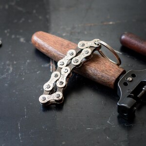 May include: A silver bike chain keychain with a wooden handle and a metal ring. The chain is made of multiple links and has the text "KMC" printed on each link.