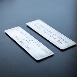 May include: Two rectangular silver-toned metal bookmarks with rounded corners. One bookmark is engraved with the text: A dad like no other Happy Father's Day. The other bookmark is engraved with the text: The best is yet to come Love Mom and Dad.