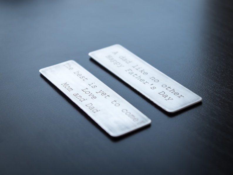 May include: Two rectangular silver-toned metal bookmarks with rounded corners. One bookmark is engraved with the text: A dad like no other Happy Father's Day. The other bookmark is engraved with the text: The best is yet to come Love Mom and Dad.