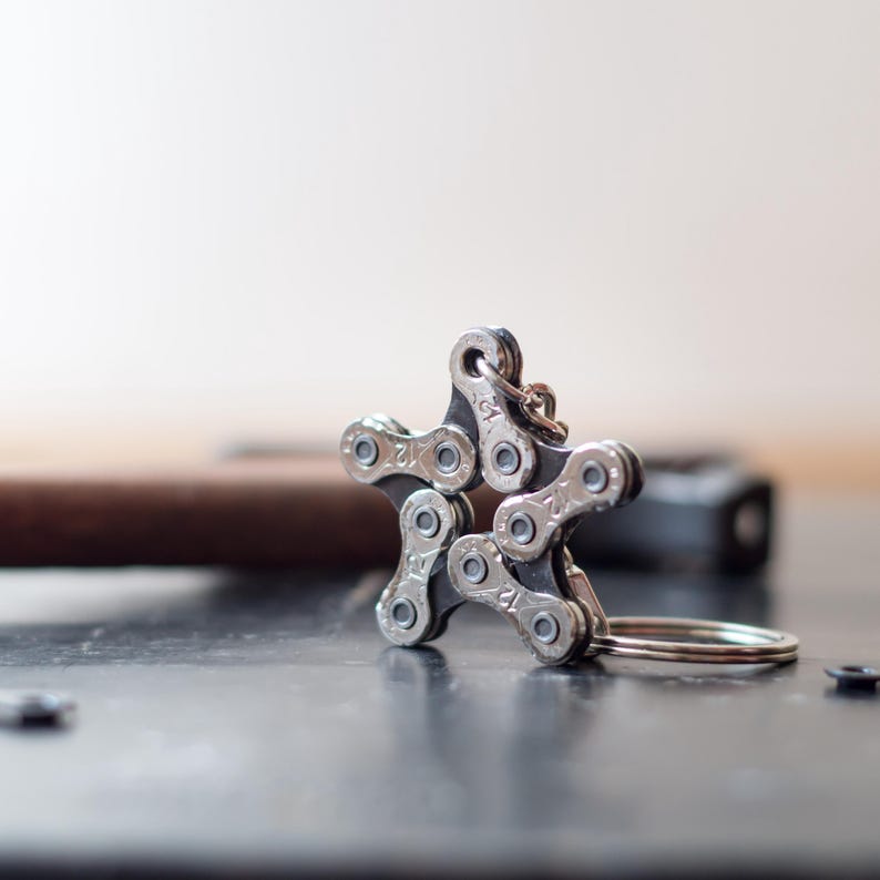May include: A silver star-shaped keychain made from a bicycle chain. The keychain has a silver ring attached to it.