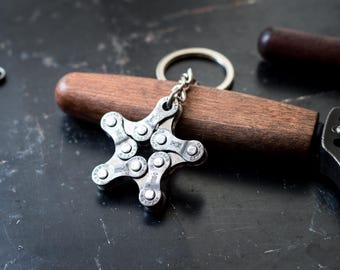 Puede incluir: Un llavero de estrella plateado hecho de una cadena de bicicleta. El llavero está unido a un anillo de llave plateado.