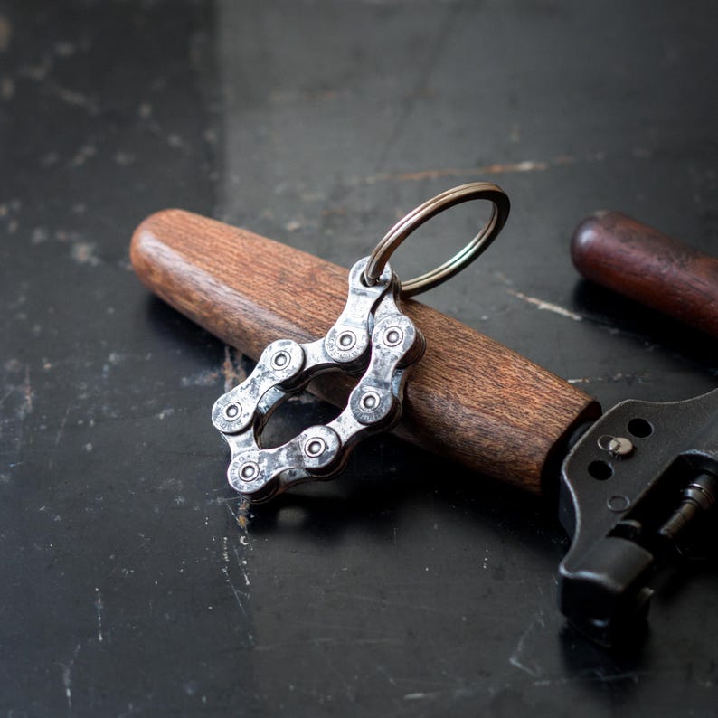 May include: A silver keychain shaped like a bicycle chain with a silver ring. The keychain is lying on a wooden surface.