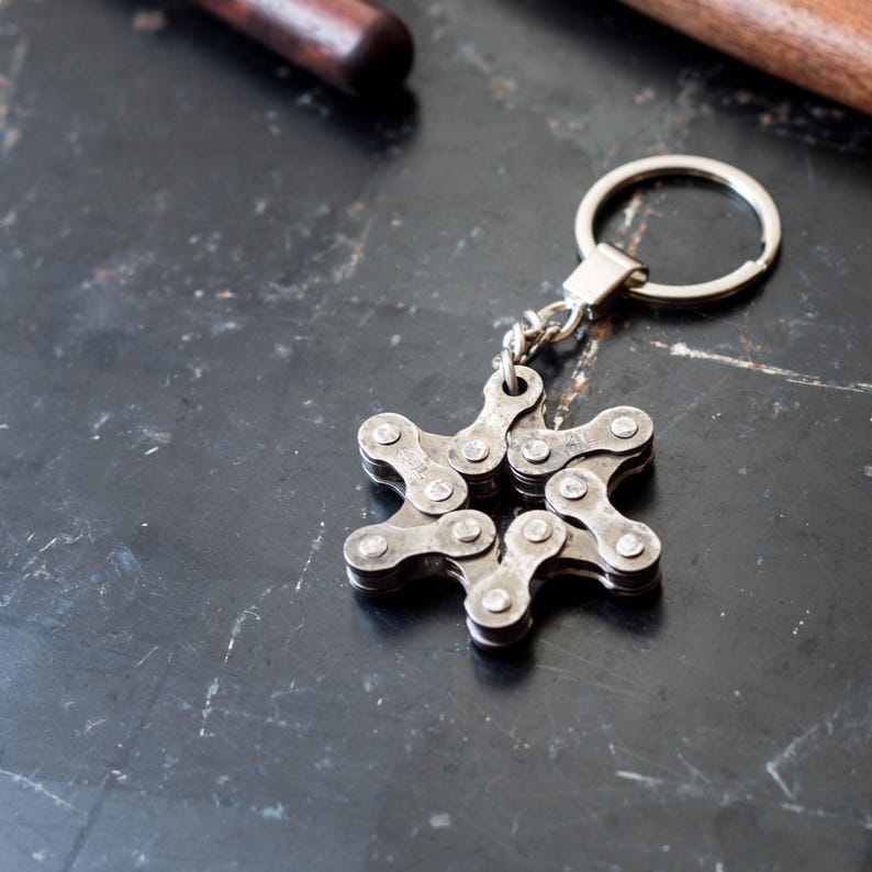 May include: A silver keychain shaped like a star, made from linked bicycle chain pieces. The keychain has a silver ring attached to it.