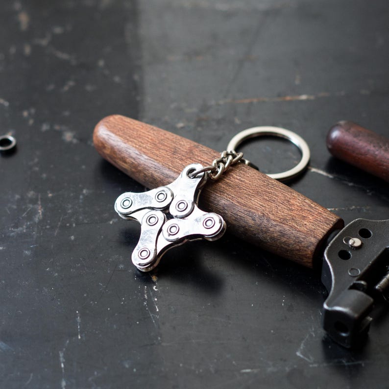 May include: A silver keychain shaped like a star made from bike chain links. The keychain is attached to a brown wooden handle with a silver ring.