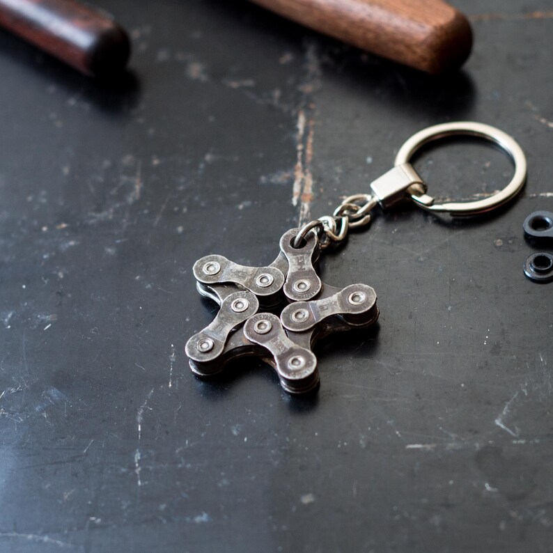 May include: A silver star-shaped keychain made from a bicycle chain. The keychain is attached to a silver ring.