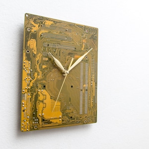 May include: A clock made from a circuit board with gold-colored traces and white clock hands.