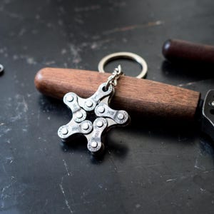 May include: A silver star-shaped keychain made from a bicycle chain. The keychain is attached to a silver key ring.