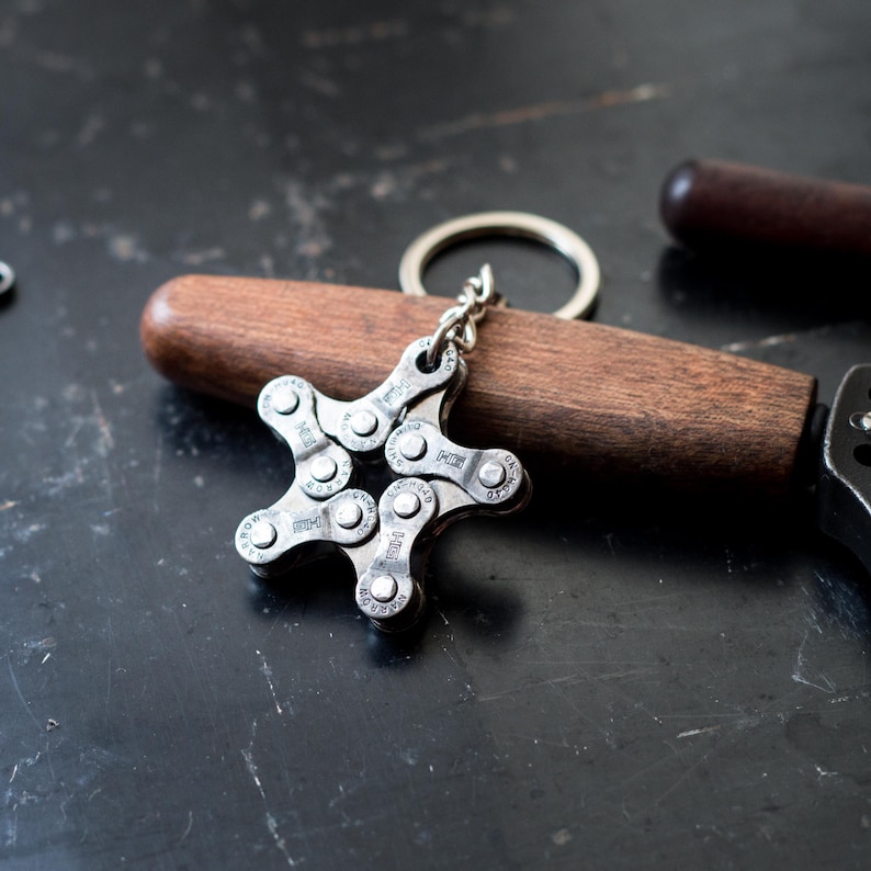 May include: A silver star-shaped keychain made from a bicycle chain. The keychain is attached to a silver key ring.