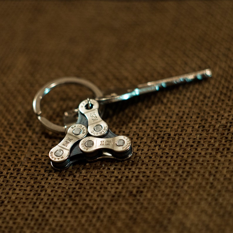 May include: A silver key chain with a triangular bike chain link charm. The chain link has the words "IGSI" and "Shimano" printed on it.