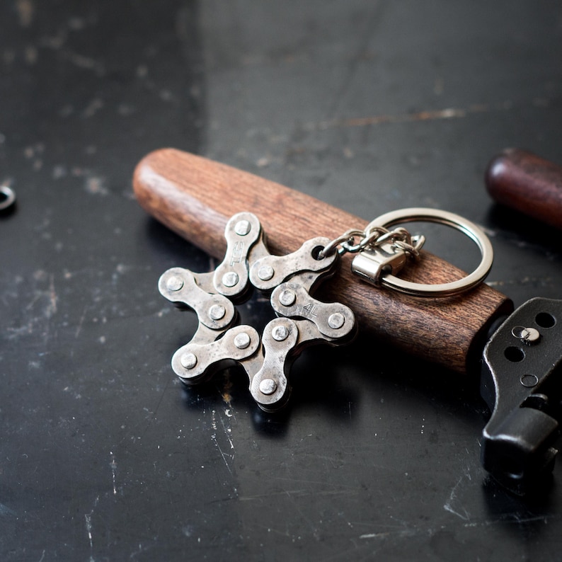 May include: A silver bike chain keychain shaped like a star. The keychain is attached to a brown wooden handle and a silver key ring.