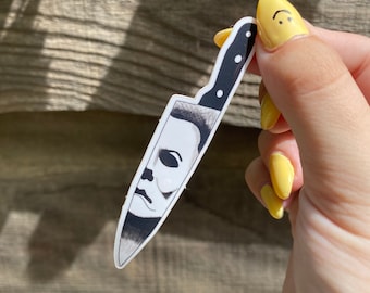 Pode incluir: Um adesivo branco de uma faca com cabo preto. A lâmina da faca tem uma imagem em preto e branco da máscara de Michael Myers dos filmes Halloween.