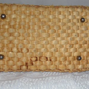 K&ouml;nnte beinhalten: Eine geflochtene Strohtasche in hellbrauner Farbe mit vier silbernen Metallakzenten.