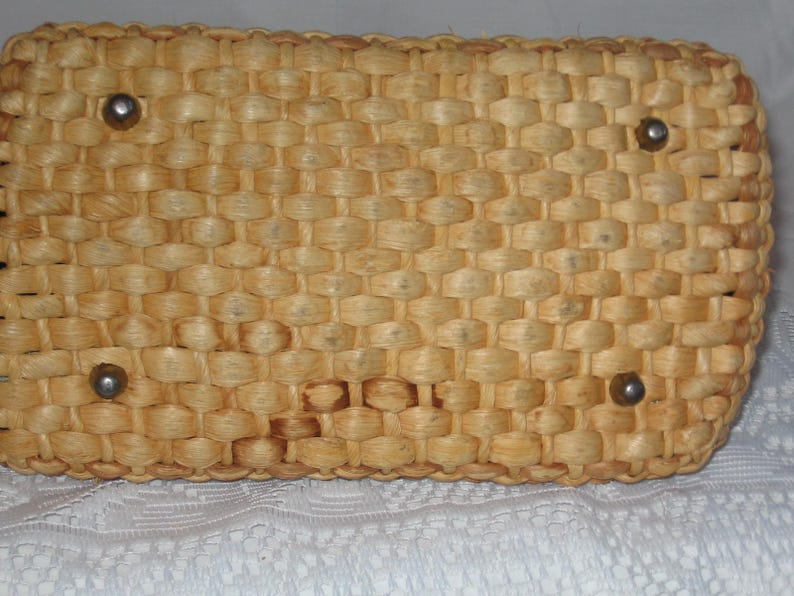 K&ouml;nnte beinhalten: Eine geflochtene Strohtasche in hellbrauner Farbe mit vier silbernen Metallakzenten.