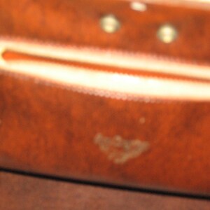 K&ouml;nnte beinhalten: Nahaufnahme einer braunen Lederb&ouml;rse mit einem Rei&szlig;verschlussfach und einem kleinen gepr&auml;gten Logo. Die B&ouml;rse hat einen abgenutzten, Vintage-Look.