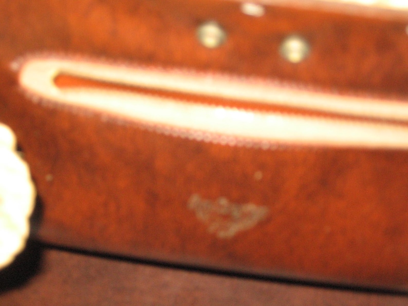K&ouml;nnte beinhalten: Nahaufnahme einer braunen Lederb&ouml;rse mit einem Rei&szlig;verschlussfach und einem kleinen gepr&auml;gten Logo. Die B&ouml;rse hat einen abgenutzten, Vintage-Look.
