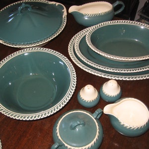 Può includere: Un set di stoviglie in ceramica verde acqua con bordo bianco. Il set comprende una grande ciotola da portata, una ciotola più piccola, una salsiera, una zuccheriera e due saliere.